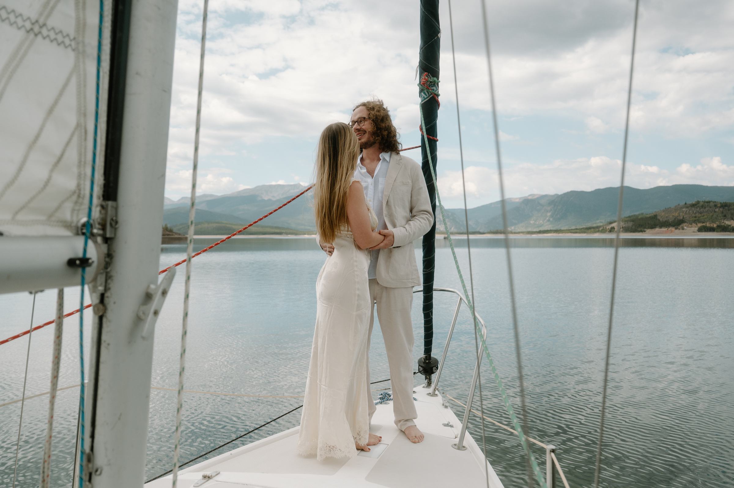 Lauren and Christopher embracing on the bow of a sailboat, mountains across the lake